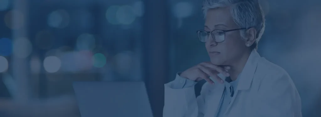 A woman in a lab coat is focused on her laptop, engaged in work or research in a laboratory setting